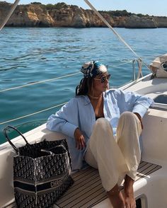 a woman sitting on the deck of a sailboat with her purse and handbag