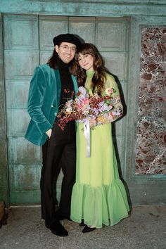 a man and woman standing next to each other in front of a wooden door holding flowers