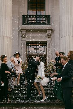 a newly married couple kissing in front of an old building with confetti falling all around them