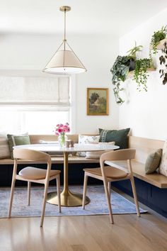 a dining room table with two chairs and a bench in front of the window, along with potted plants