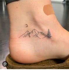 a small tattoo on the foot of a person with mountains and trees in the background