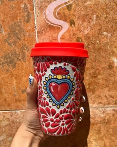 a hand holding a red and white coffee cup with a heart painted on the side