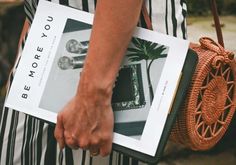 a person holding a book with a plant in it and a purse on their back