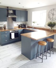 a kitchen with blue cabinets and wooden counter tops in front of a clock on the wall