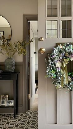 a door with a wreath hanging on it's side next to a table and mirror