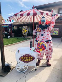 a person dressed as a clown standing next to a candy machine with an umbrella over it