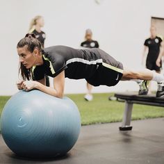 a woman is doing push ups on an exercise ball while other people are in the background