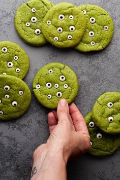 green cookies with googly eyes are being held by a person's hand on a gray surface