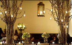 two vases filled with flowers and candles on top of a table covered in branches