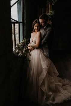 a bride and groom embracing in front of a window