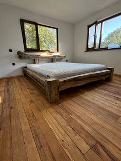 a bed sitting on top of a wooden floor in a bedroom next to two windows