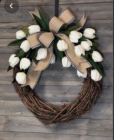 a wreath with white tulips and burlock on it hanging on a wooden wall