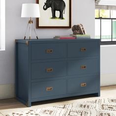 a blue dresser with an elephant painting on the wall above it and a lamp next to it