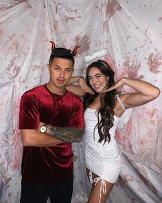 a man and woman posing for a photo in front of a white backdrop with devil horns on their head