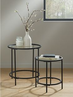 two tables with vases on them sitting in front of a window, one is black and the other is white