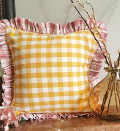 a yellow and white gingham pillow sitting on top of a table next to a vase