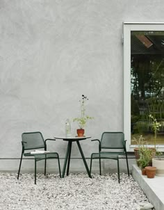 two chairs and a table in front of a white wall with an open glass door