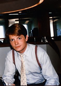 a man wearing suspenders and a tie sitting in front of a computer desk with his hands on his hips