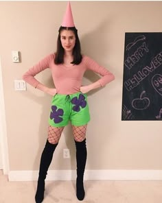 a woman in green shorts and a pink hat standing next to a chalkboard with writing on it