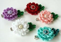 four different colored flower hair clips on a white surface with pearls in the center, and two are attached to clip holders