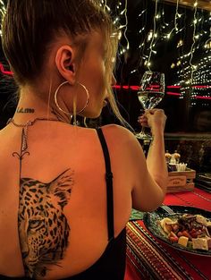 a woman with a leopard tattoo on her back holding a wine glass and looking at the camera