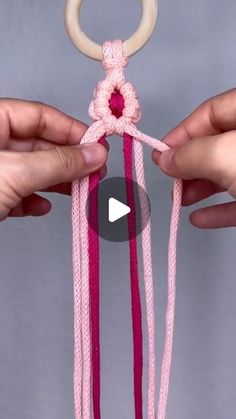 two hands holding an object that looks like a ring with pink thread and beads on it