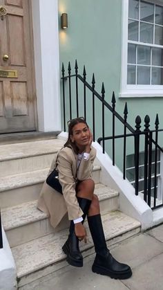 a woman is sitting on the steps in front of a door and wearing black boots