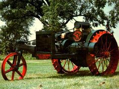 an old fashioned tractor sitting on top of a lush green field next to a tree