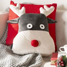 a reindeer pillow sitting on top of a couch next to a coffee cup and christmas decorations