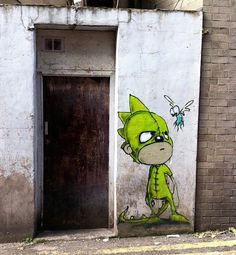 a green cat painted on the side of a building next to a brick wall and door