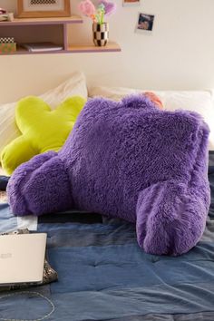 a large purple teddy bear laying on top of a bed next to a laptop computer