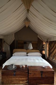 a bed sitting under a white canopy next to two wooden boxes on top of a hard wood floor