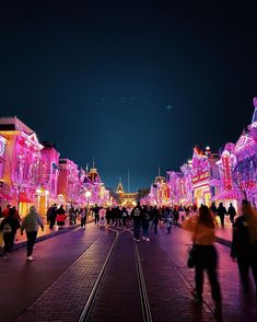 many people are walking down the street in front of some buildings with lights on them