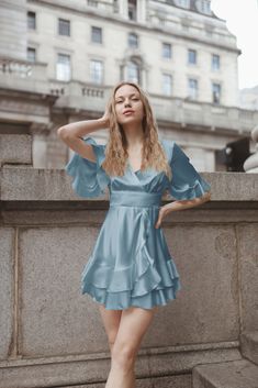 This romantic satin dress will be handmade bespoke for you in London. Cut from luxury fabric, wrinkle-proof, and drapes magnificently along with the silhouette. It features a deep V neck, a side tie fastening,  ruffles, flared skirt, loose sleeves, and a fitted silhouette. This design is super versatile and easy to wear, mixing the quirks of bewitching glam with effortless chic. Perfect for an alfresco lunch with friends, or a romantic city-stroll date. - Dress is partially lined - Mini Length - Satin Ruffle Dress For Wedding Guest, Satin Tiered Dress With Ruffles, Satin Mini Dress With Ruffles For Wedding, Tiered Satin Dress With Ruffles, Chic Tiered Satin Dresses, Summer Wedding Guest Dress With Satin Finish, Blue Ruffled Mini Dress For Wedding, Elegant Light Blue Satin Dress, Satin Ruffled Mini Dress For Wedding