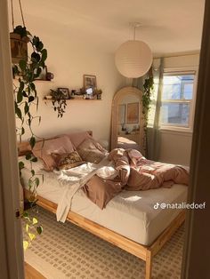 an unmade bed sitting in a bedroom next to a mirror and potted plant