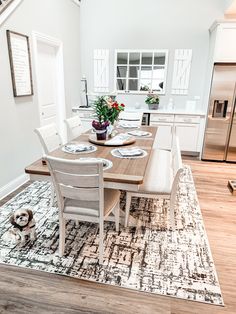 a dining room table with chairs and a dog sitting on the rug in front of it