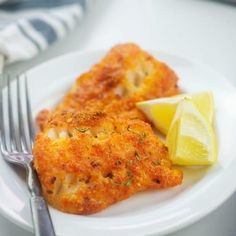 a white plate topped with two pieces of fried chicken next to a slice of lemon