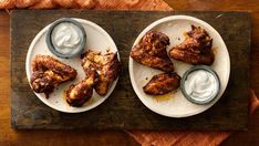 two plates with chicken wings and ranch dips on them sitting on a wooden table