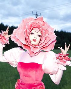 a woman in a pink dress with a large flower on her head and hands out