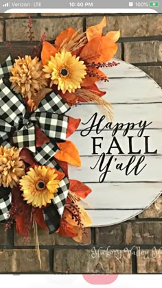 a happy fall wreath with sunflowers and plaid ribbon on a brick wall in front of a sign that says happy fall