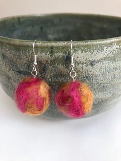 two orange and pink balls are hanging from silver earwires on a green bowl