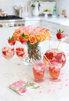 a table topped with glasses filled with liquid and flowers in vases next to each other