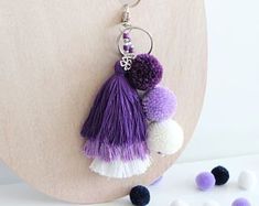 two tasselled pom poms hanging from a hook on a piece of wood