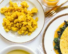 two plates with breakfast foods on them next to cups and spoons, one has scrambled eggs and the other has spinach