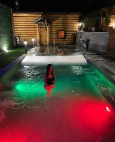 a woman standing in the middle of a pool with red and green lights on it