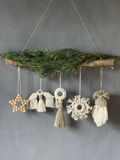 an assortment of ornaments hanging from a tree branch on a gray wall with pine needles