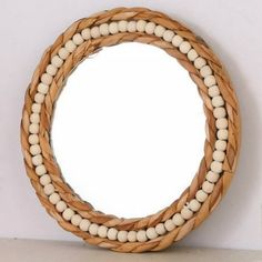 a round mirror sitting on top of a white wall next to a wooden frame with beads