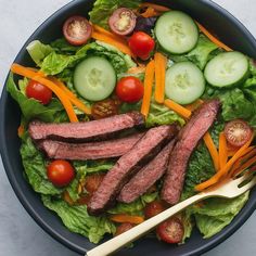 a salad with steak, carrots, cucumbers and tomatoes in a bowl