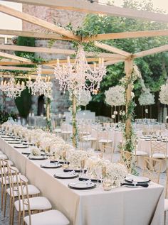 an outdoor wedding reception with chandeliers and white flowers on the table, surrounded by greenery