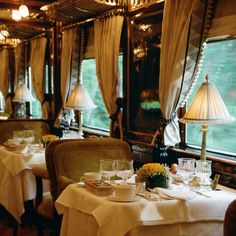 a dining car on a train with white tablecloths and flowers in vases